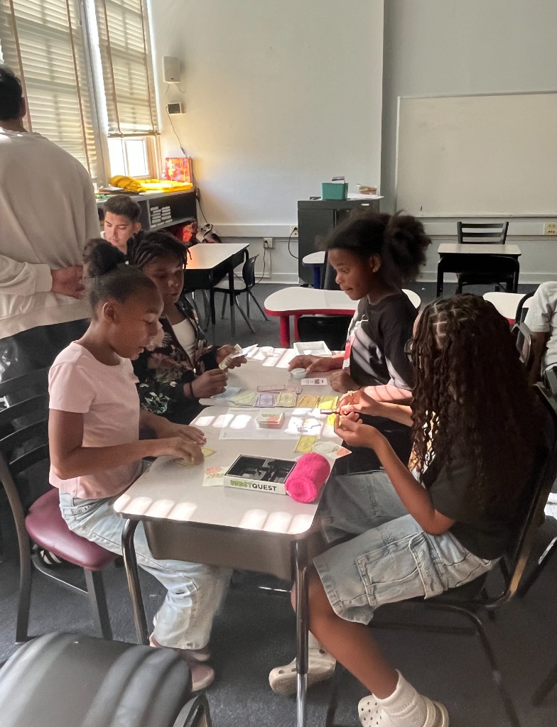 Students playing InvestQuest at a sunlit classroom table