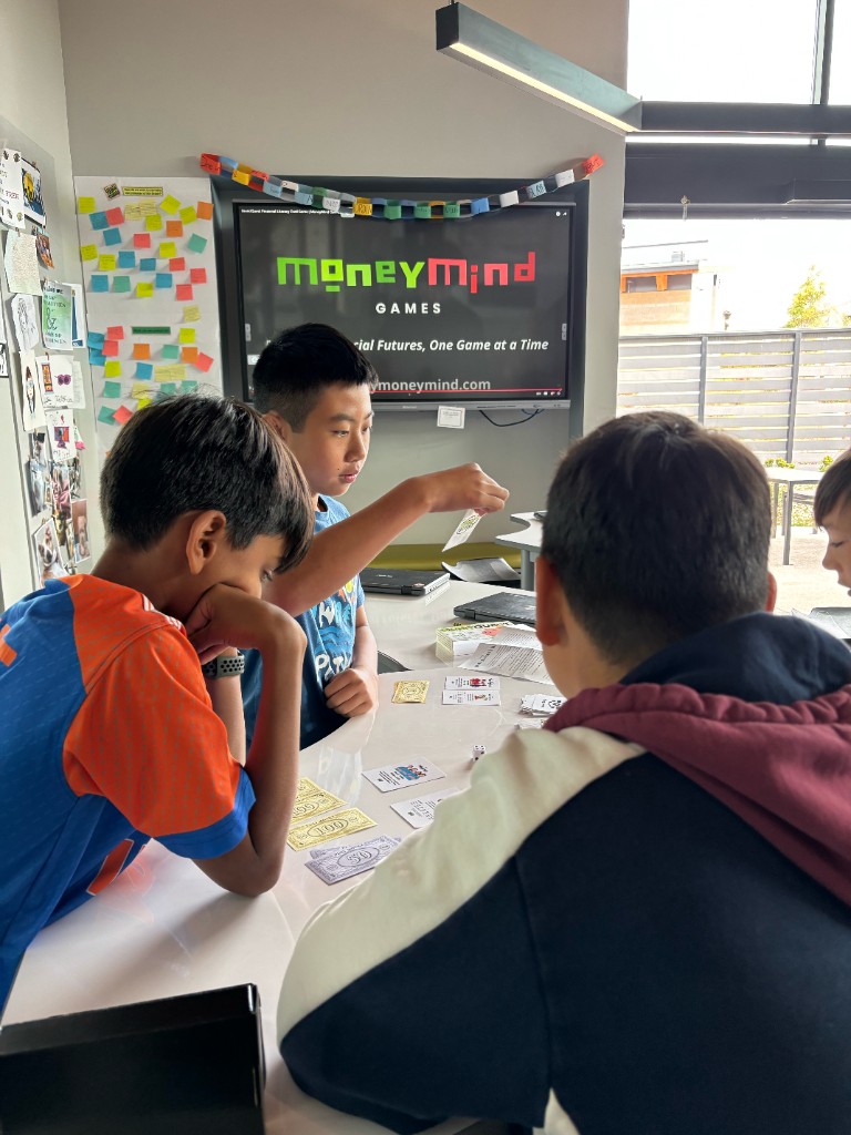 Students playing InvestQuest with a MoneyMind lesson on the classroom screen