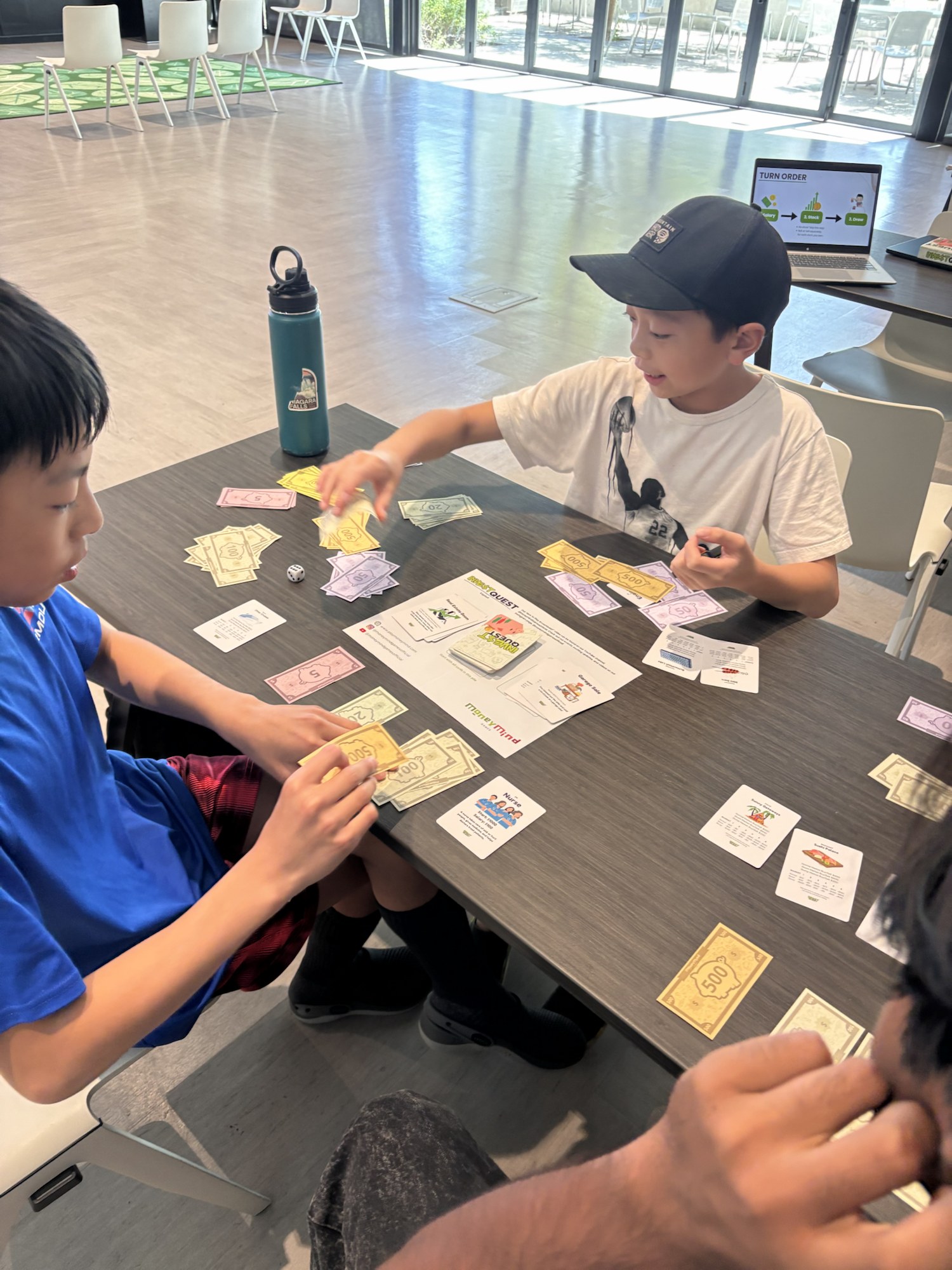 Kids playing InvestQuest at a table with play money and cards